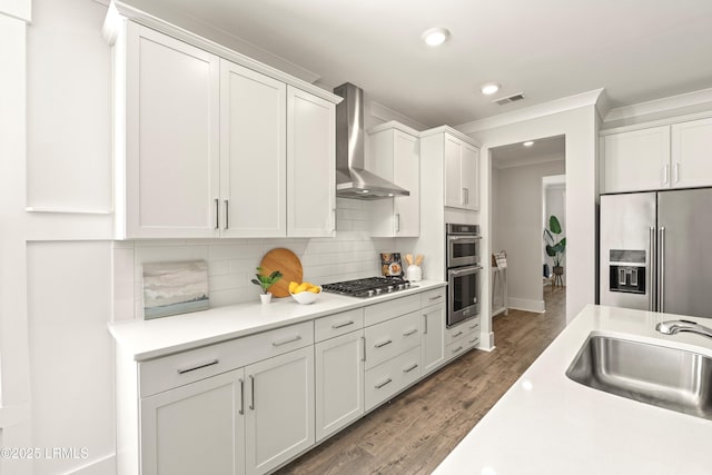 kitchen with decorative backsplash, stainless steel appliances, light countertops, wall chimney range hood, and a sink