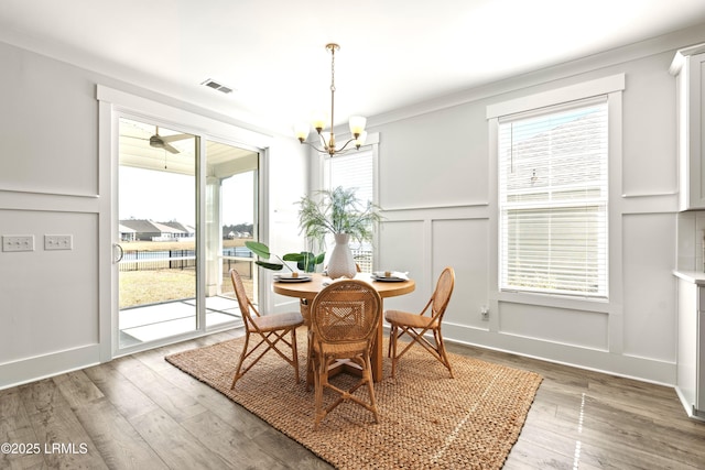 dining room with wood-type flooring, a notable chandelier, a decorative wall, and visible vents