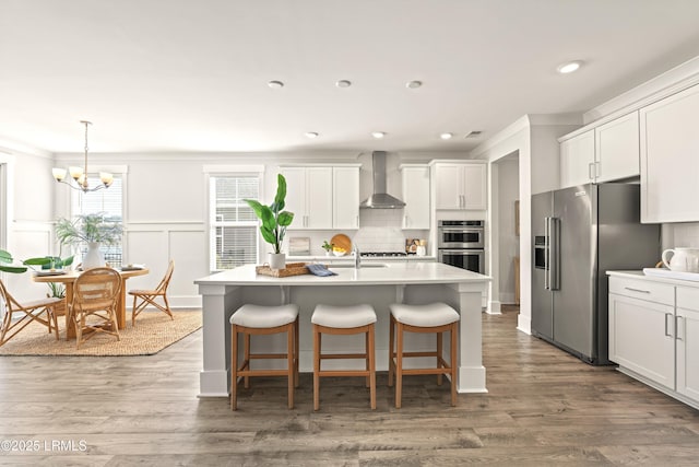 kitchen with ornamental molding, wall chimney range hood, appliances with stainless steel finishes, and decorative backsplash