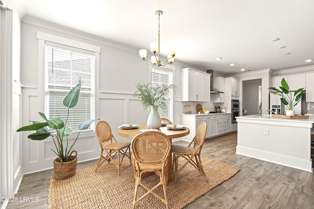 dining space featuring light wood-type flooring, a chandelier, a decorative wall, and crown molding