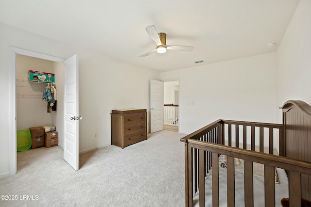 bedroom featuring light carpet, a crib, a closet, and ceiling fan