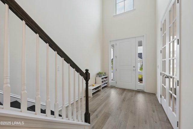 entryway with french doors, a healthy amount of sunlight, light wood-type flooring, and a towering ceiling