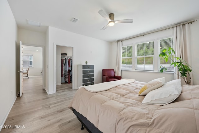 bedroom featuring a walk in closet, light hardwood / wood-style floors, a closet, and ceiling fan