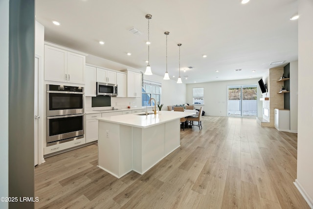 kitchen featuring an island with sink, sink, white cabinets, hanging light fixtures, and stainless steel appliances