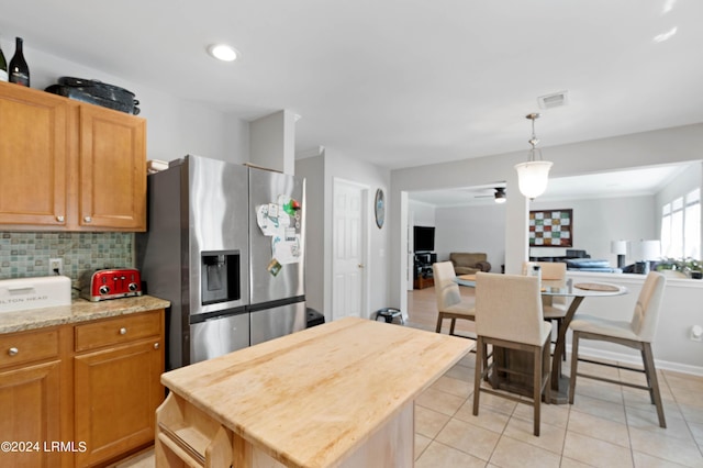 kitchen with light tile patterned floors, hanging light fixtures, stainless steel refrigerator with ice dispenser, a kitchen island, and decorative backsplash