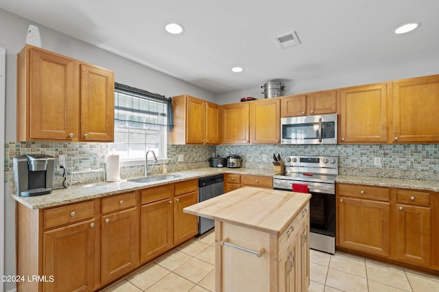 kitchen with a kitchen island, appliances with stainless steel finishes, sink, light tile patterned floors, and light stone counters