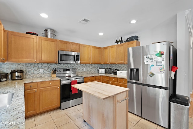 kitchen featuring light tile patterned flooring, a center island, stainless steel appliances, light stone countertops, and decorative backsplash