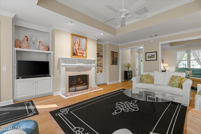 living room featuring hardwood / wood-style flooring, crown molding, a fireplace, and a tray ceiling