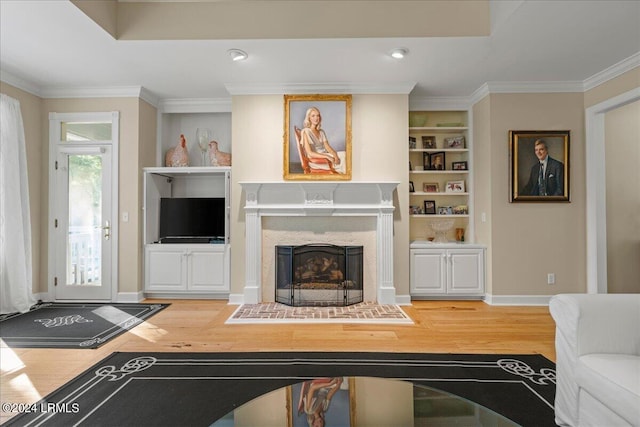 living room featuring built in shelves, wood-type flooring, ornamental molding, and a high end fireplace