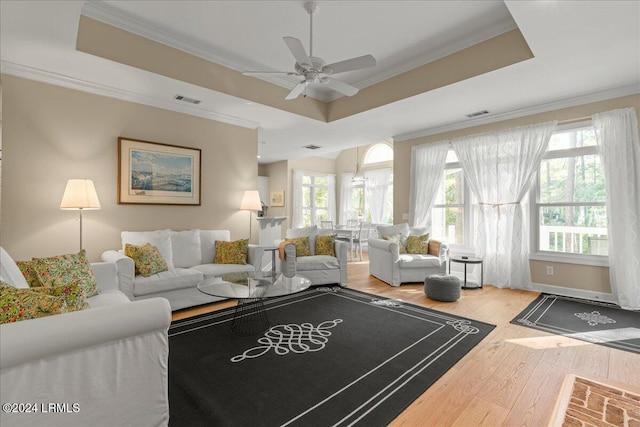 living room with a raised ceiling, ornamental molding, hardwood / wood-style floors, and ceiling fan