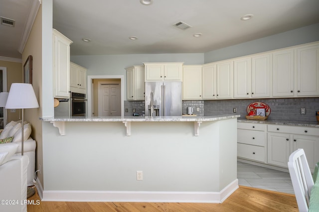 kitchen with high end fridge, white cabinetry, light wood-type flooring, and a kitchen bar