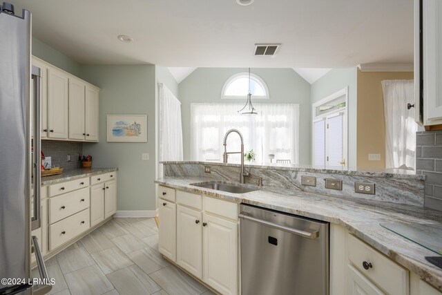 kitchen featuring lofted ceiling, sink, appliances with stainless steel finishes, tasteful backsplash, and light stone countertops