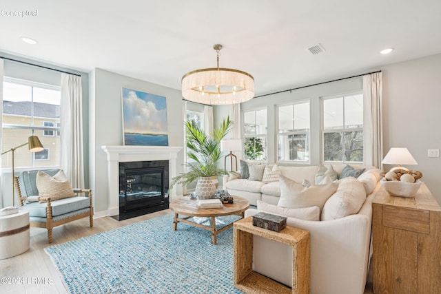living area with visible vents, wood finished floors, a wealth of natural light, and an inviting chandelier