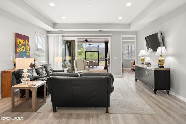 living area featuring recessed lighting, baseboards, light wood-type flooring, a raised ceiling, and a ceiling fan
