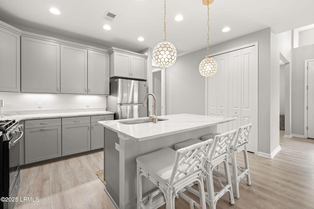 kitchen with stainless steel appliances, gray cabinetry, light wood-type flooring, and a sink