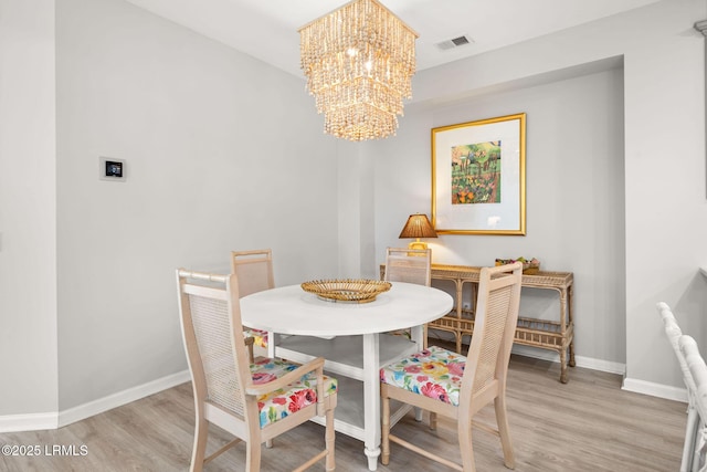 dining room featuring light wood-style flooring, visible vents, a notable chandelier, and baseboards