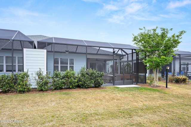 rear view of house with glass enclosure, a ceiling fan, and a yard