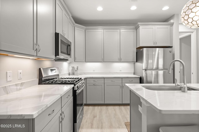kitchen featuring light stone countertops, light wood-style flooring, stainless steel appliances, a sink, and gray cabinetry