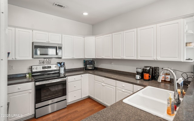 kitchen with appliances with stainless steel finishes, sink, dark wood-type flooring, and white cabinets