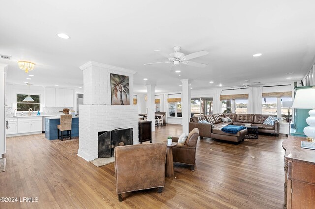 living room featuring sink, light hardwood / wood-style flooring, ceiling fan, a fireplace, and decorative columns