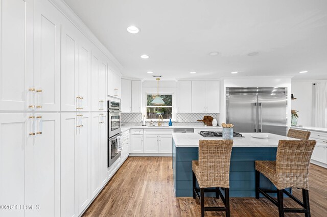 kitchen featuring appliances with stainless steel finishes, a breakfast bar, a kitchen island, white cabinetry, and hanging light fixtures