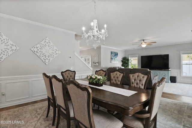 dining room featuring a wainscoted wall, stairway, wood finished floors, ceiling fan with notable chandelier, and ornamental molding