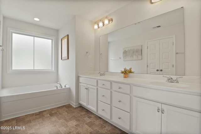 full bath with a sink, a garden tub, visible vents, double vanity, and stone finish flooring
