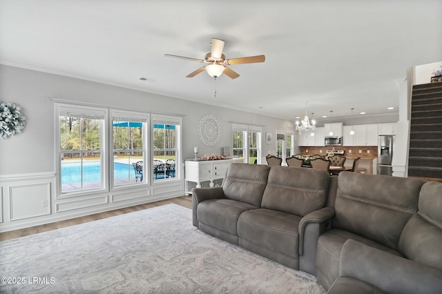 living area with ornamental molding, wood finished floors, ceiling fan with notable chandelier, and wainscoting