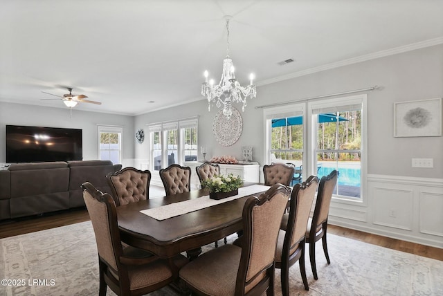 dining room with crown molding, ceiling fan with notable chandelier, a wainscoted wall, visible vents, and wood finished floors