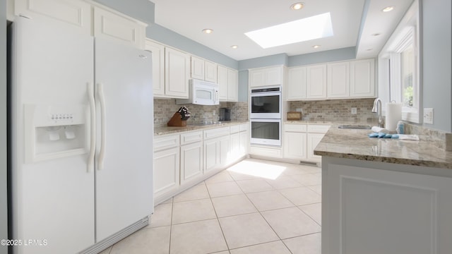 kitchen with sink, tasteful backsplash, a skylight, white appliances, and white cabinets