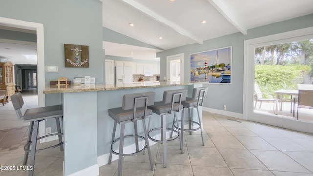 kitchen featuring a breakfast bar area, vaulted ceiling with beams, kitchen peninsula, white refrigerator with ice dispenser, and white cabinets