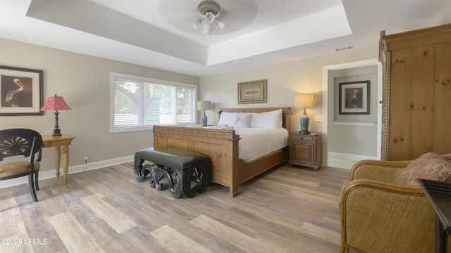 bedroom with light hardwood / wood-style floors, ceiling fan, and a tray ceiling