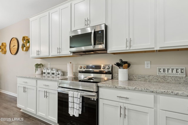 kitchen with stainless steel appliances, white cabinetry, wood finished floors, light stone counters, and baseboards