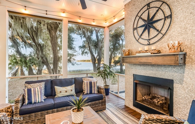 sunroom / solarium with a water view, track lighting, exterior fireplace, and ceiling fan