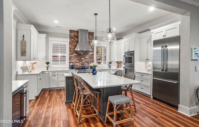 kitchen with white cabinets, hanging light fixtures, a center island, stainless steel appliances, and wall chimney exhaust hood