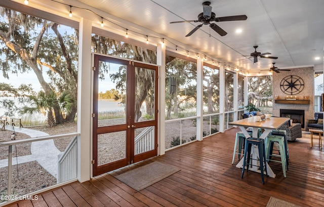 sunroom with a fireplace, ceiling fan, and a water view