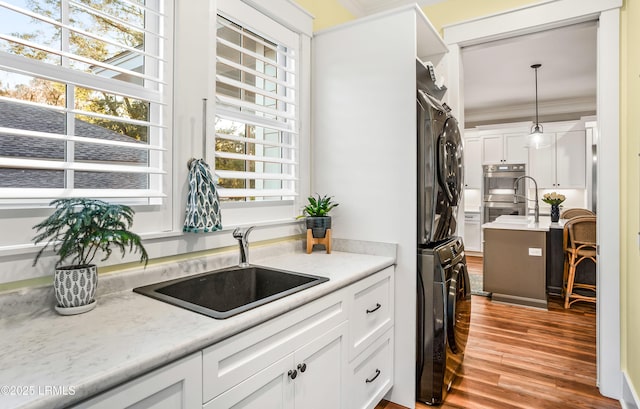 kitchen with pendant lighting, stacked washer / drying machine, crown molding, and sink