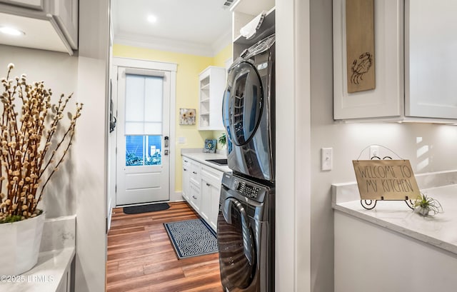 clothes washing area featuring cabinets, ornamental molding, stacked washing maching and dryer, and dark hardwood / wood-style flooring