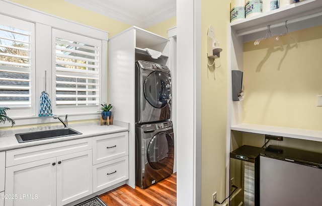 laundry area with ornamental molding, stacked washer / dryer, light hardwood / wood-style floors, and sink