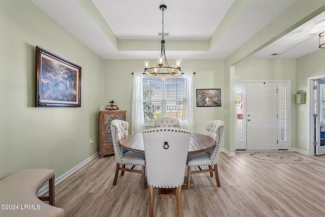 dining area with a raised ceiling, baseboards, light wood finished floors, and an inviting chandelier