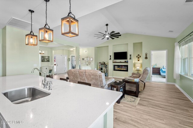 kitchen with decorative light fixtures, lofted ceiling, sink, light stone countertops, and light hardwood / wood-style flooring