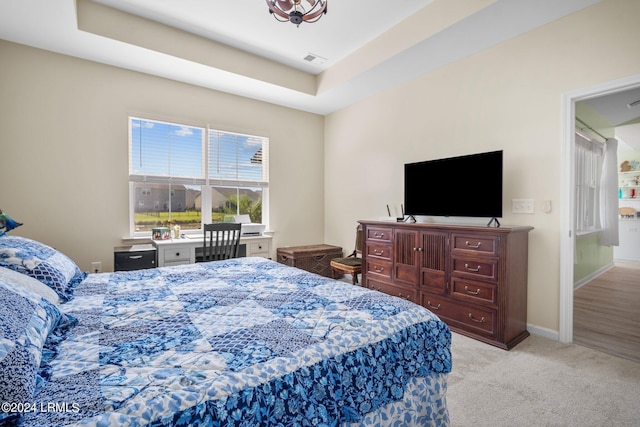 bedroom with a tray ceiling, light carpet, visible vents, and baseboards