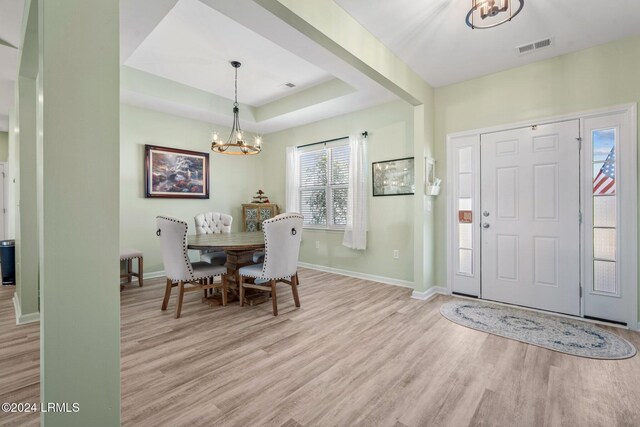 entrance foyer with visible vents, a tray ceiling, a notable chandelier, and wood finished floors