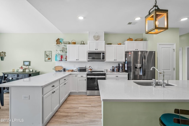 kitchen with light wood finished floors, appliances with stainless steel finishes, white cabinetry, a sink, and a peninsula