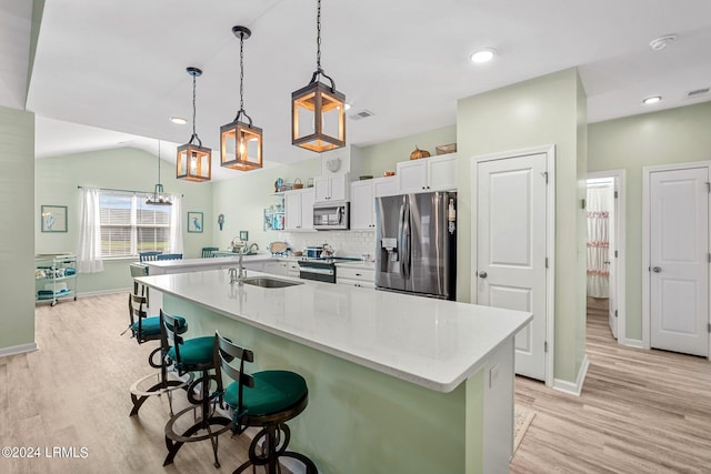 kitchen with light wood-style flooring, stainless steel appliances, a sink, white cabinets, and a kitchen bar