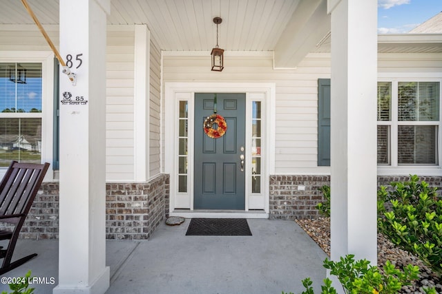 view of exterior entry featuring covered porch, stone siding, and brick siding