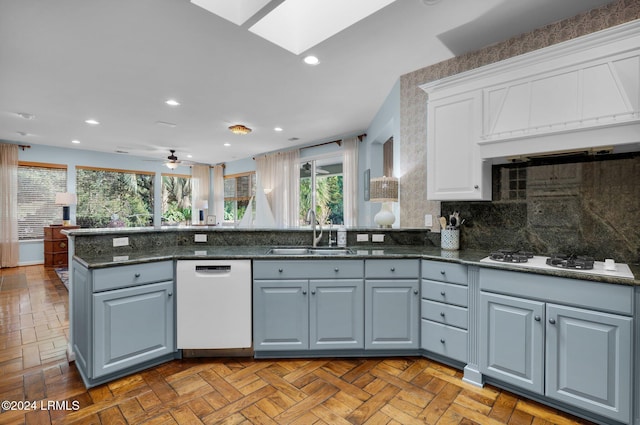 kitchen featuring a skylight, sink, white cabinets, kitchen peninsula, and white appliances