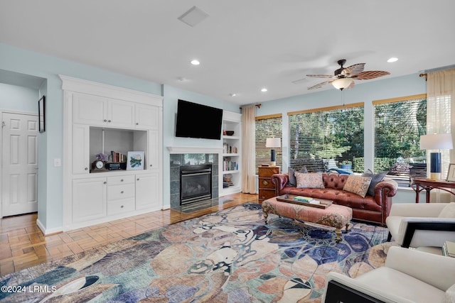 living room with a tiled fireplace, ceiling fan, built in features, and light parquet flooring