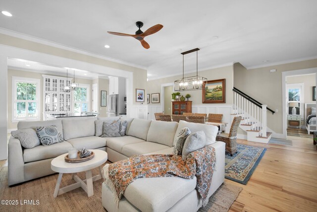 living room with ceiling fan with notable chandelier, light hardwood / wood-style flooring, and ornamental molding