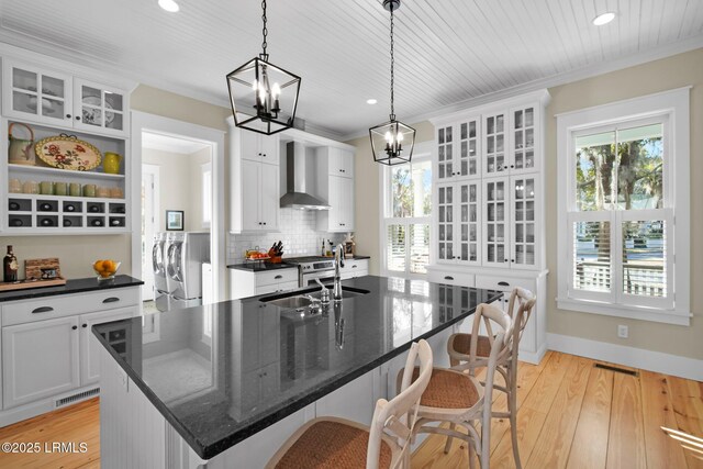 kitchen featuring an island with sink, separate washer and dryer, sink, hanging light fixtures, and wall chimney range hood